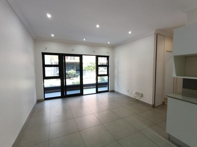 A bright, open-plan living area featuring neutral tiled floors, recessed downlighting, and large black aluminium sliding doors leading to an outdoor space.