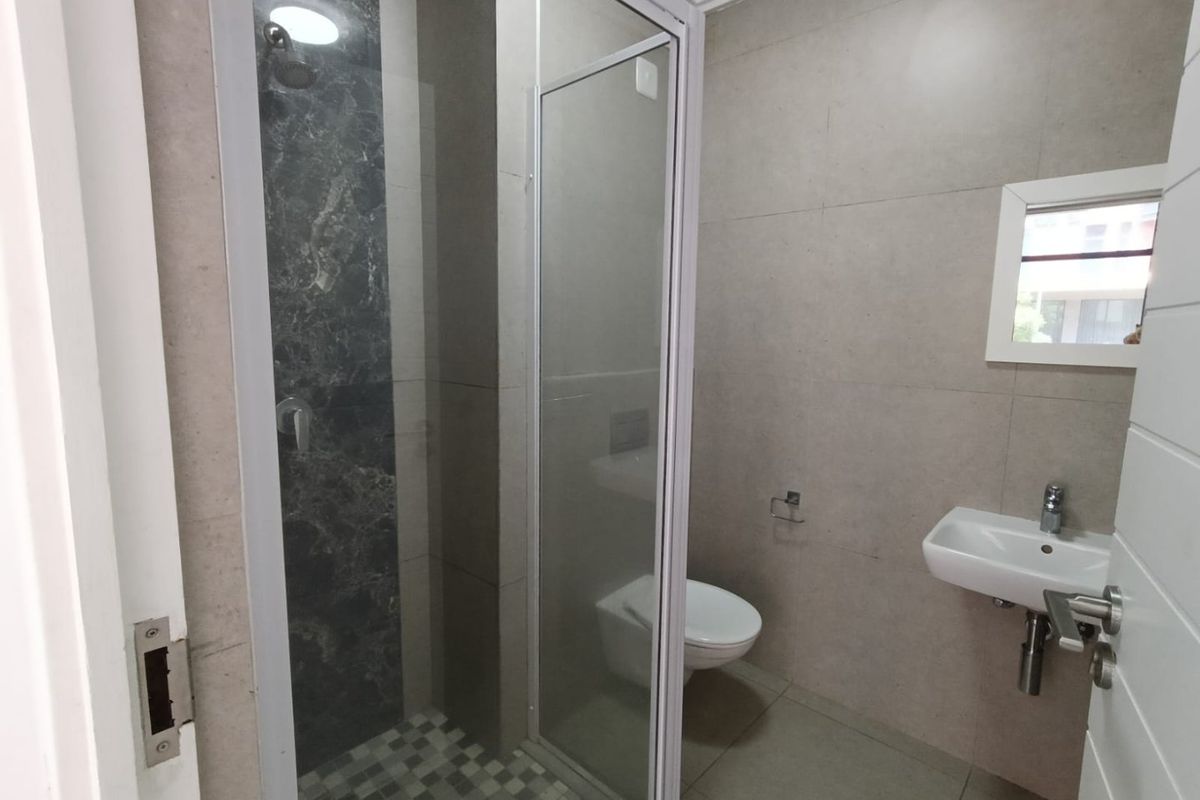 A modern, clean bathroom featuring a glass-enclosed shower, wall-mounted toilet, and a sleek basin with chrome fixtures, finished with neutral wall and floor tiles.