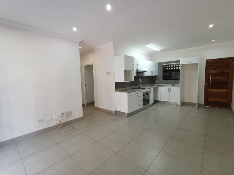 An open-plan living and kitchen area featuring modern white cabinetry, integrated appliances, tiled flooring, and recessed lighting in a clean, vacant space.