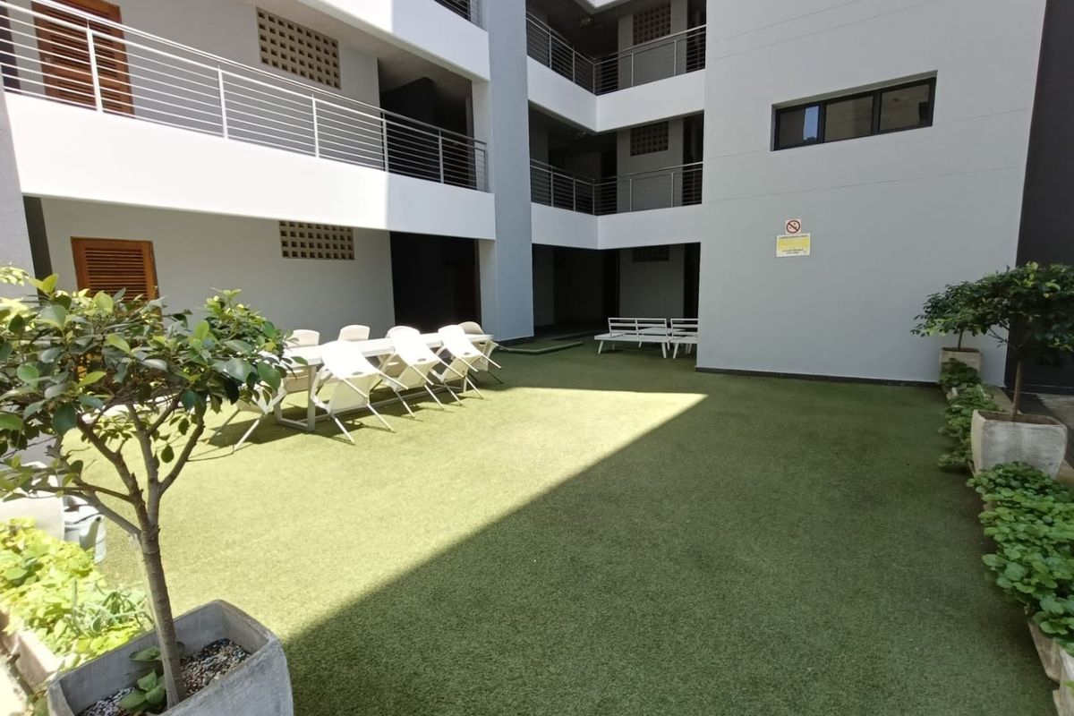 A well-maintained communal courtyard area featuring artificial turf, modern building facades, and metal balcony railings within an apartment complex.