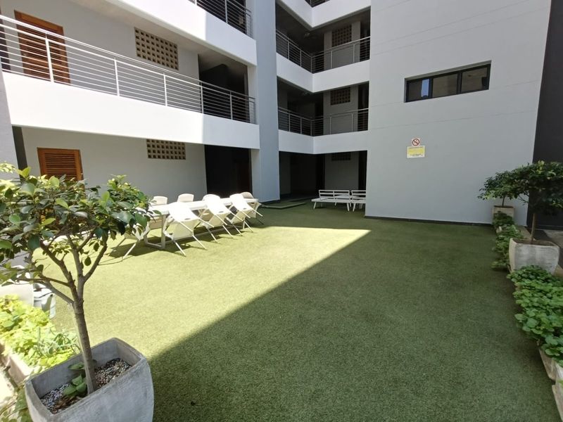 A well-maintained communal courtyard area featuring artificial turf, modern building facades, and metal balcony railings within an apartment complex.