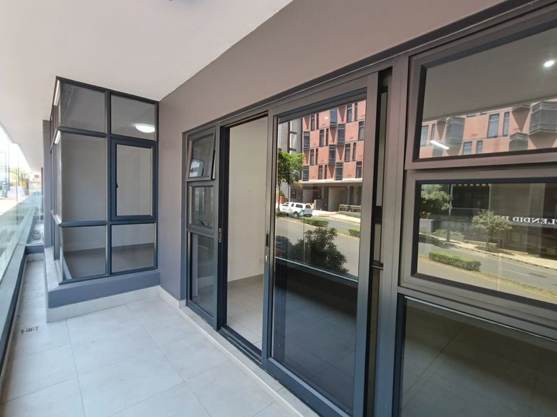 A modern, covered balcony featuring sleek aluminium sliding doors, large windows, and tiled flooring, offering a clean and contemporary outdoor living space.