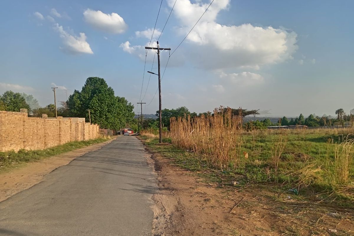 A view of the access road adjacent to the vacant residential land, featuring a brick boundary wall and existing utility infrastructure.