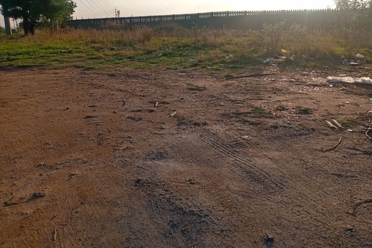A view of a vacant residential plot featuring unimproved ground and perimeter fencing.