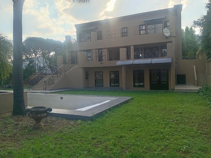 Rear view of a multi-story house featuring a swimming pool, external staircase, and balconies with wrought iron railings.