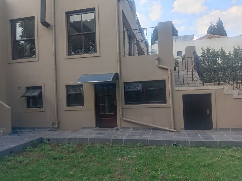 Rear exterior view of the property featuring a tiled patio, external staircase with wrought iron railings, and established garden area.