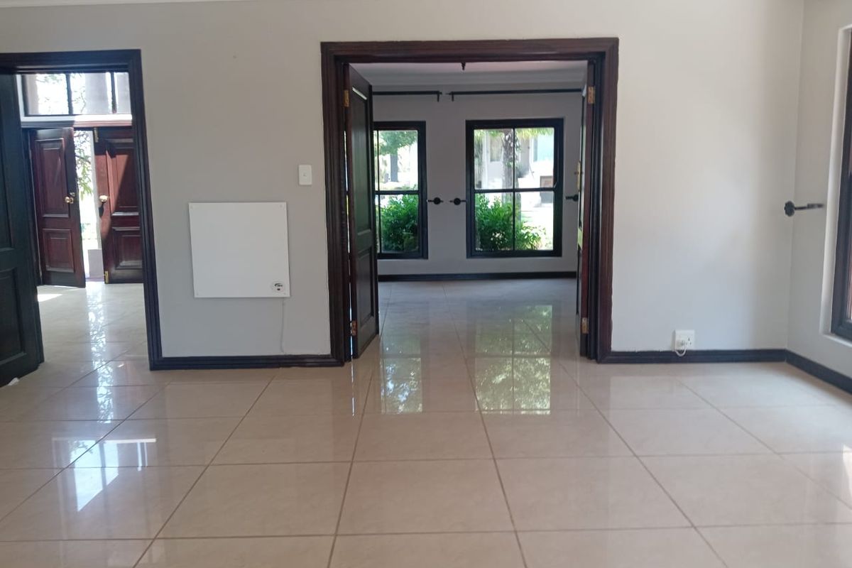 A spacious, empty living area featuring neutral tiled flooring, dark wood door frames, and a wall-mounted electric heater.