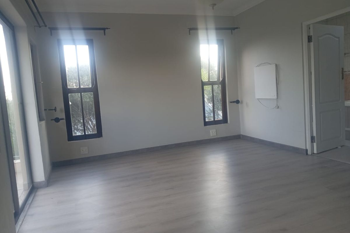A bright, empty bedroom featuring modern laminate flooring, neutral walls, and natural light through sliding glass doors and windows.