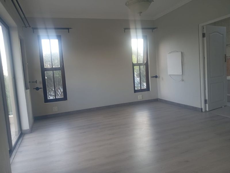 A bright, empty bedroom featuring modern laminate flooring, neutral walls, and natural light through sliding glass doors and windows.