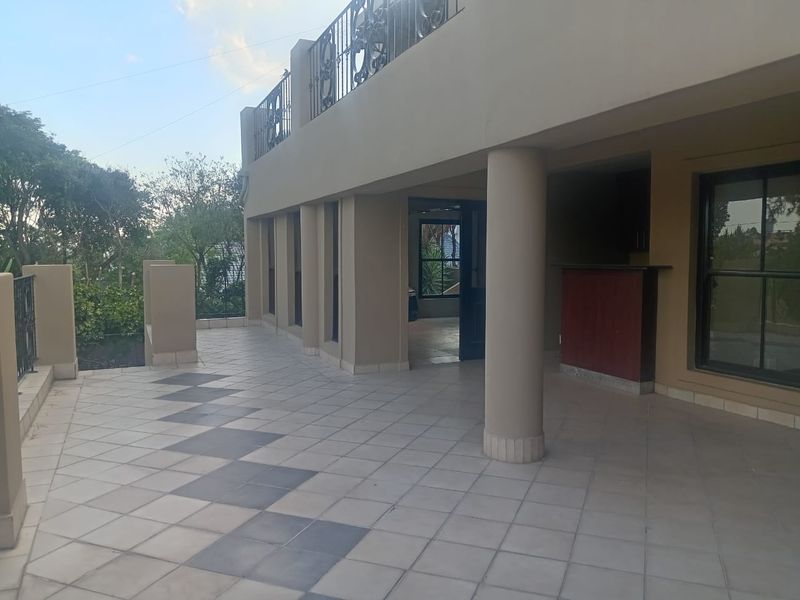 A spacious covered patio featuring tiled flooring, structural columns, and a built-in bar counter, offering a versatile outdoor entertainment area.