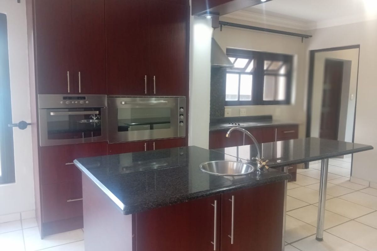 A spacious kitchen featuring dark wood cabinetry, granite countertops, a central island with a sink, and built-in stainless steel appliances.