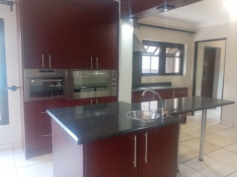 A spacious kitchen featuring dark wood cabinetry, granite countertops, a central island with a sink, and built-in stainless steel appliances.