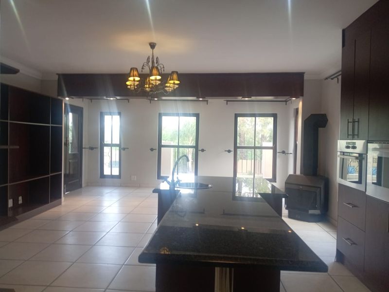 Spacious open-plan living and kitchen area featuring a large granite island, built-in oven, dark cabinetry, and a cozy wood-burning fireplace.
