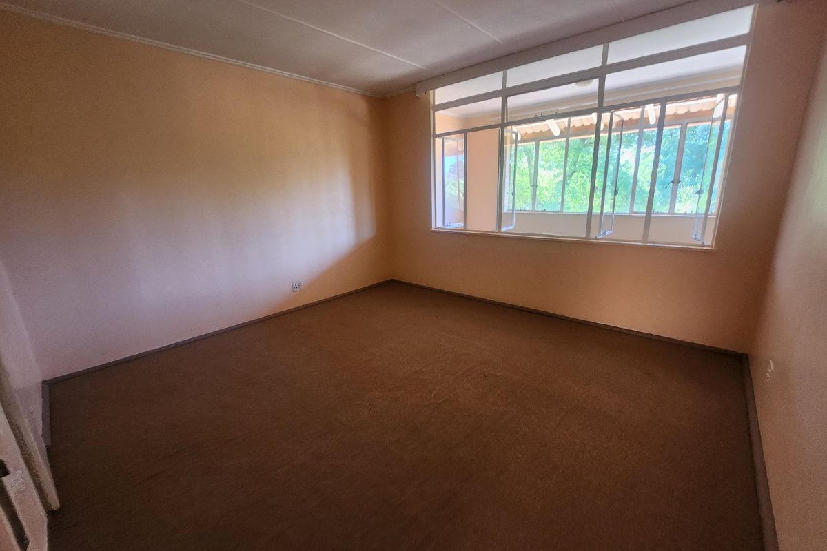 An empty bedroom featuring carpet flooring and a large window, providing a blank canvas for potential renovation and interior design updates.