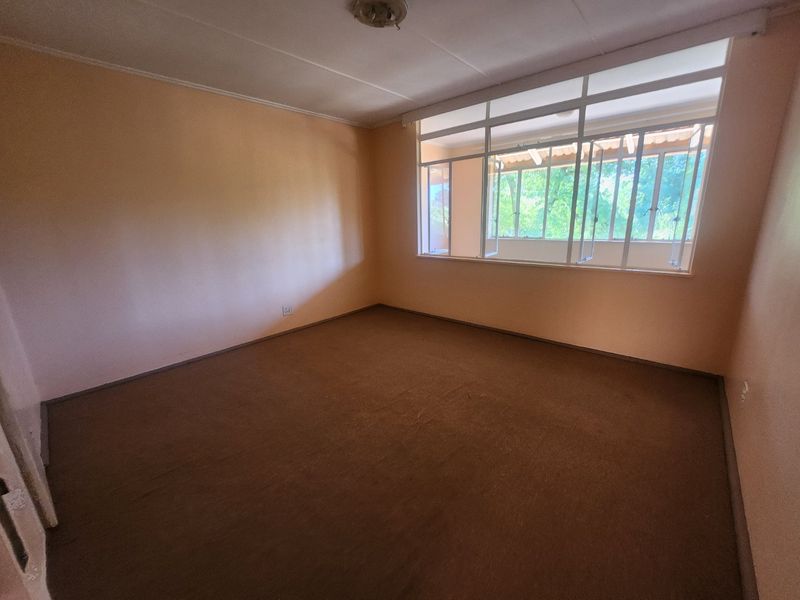 An empty bedroom featuring carpet flooring and a large window, providing a blank canvas for potential renovation and interior design updates.