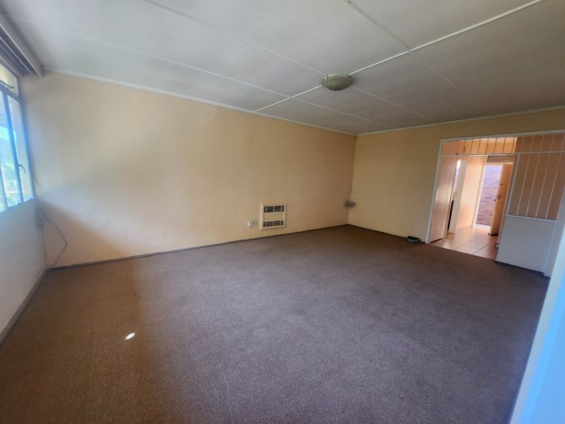 An empty, carpeted living room featuring a built-in wall heater and access to an adjacent tiled area through a security gate.