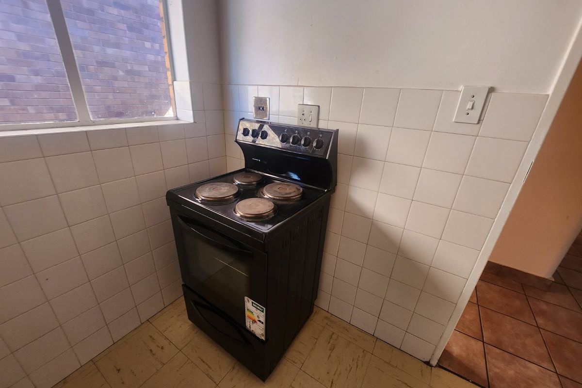 A compact kitchen area featuring a freestanding electric stove, tiled splashback, and tiled flooring, offering a functional space ready for modernization.