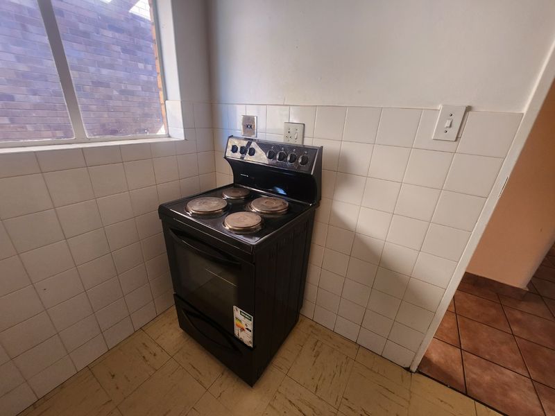 A compact kitchen area featuring a freestanding electric stove, tiled splashback, and tiled flooring, offering a functional space ready for modernization.
