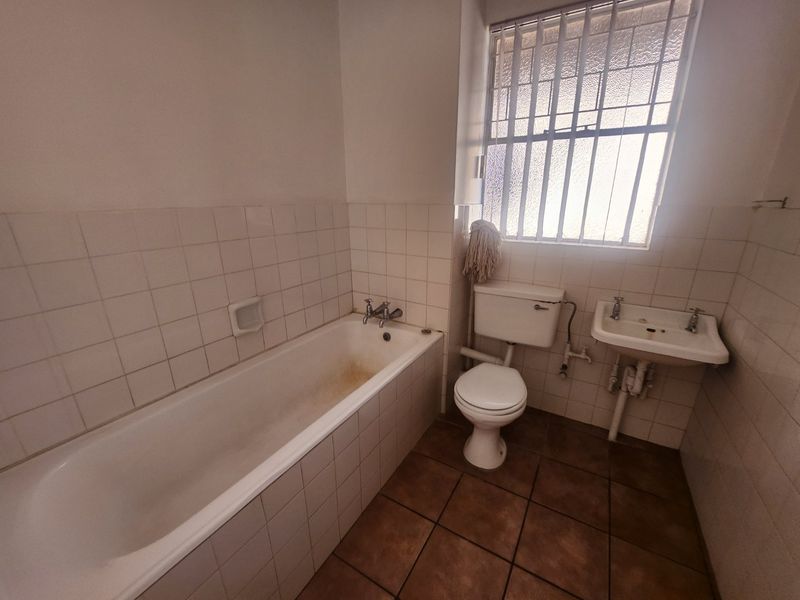A dated bathroom featuring a bathtub, toilet, and wall-mounted basin with tiled finishes, requiring cosmetic updates to modernize the space.