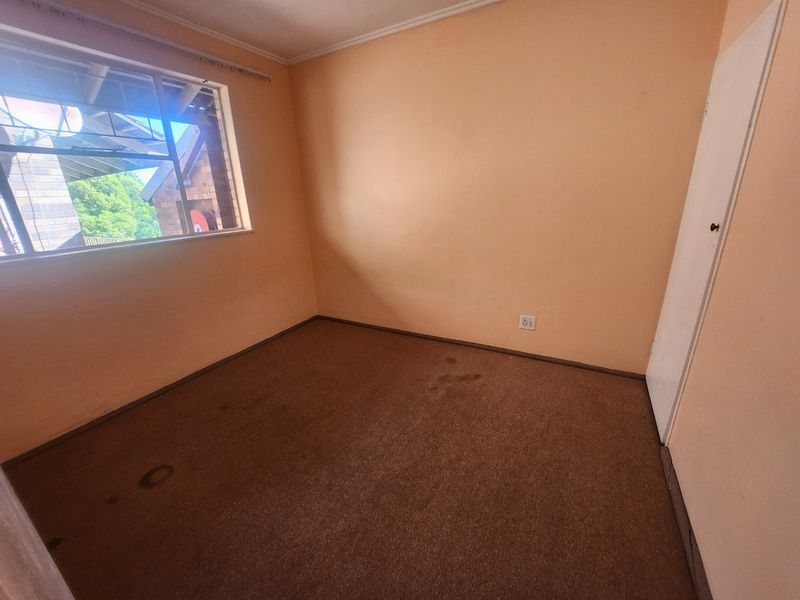 An empty bedroom featuring carpeted flooring, a built-in cupboard, and a window with natural light. The room requires cosmetic updates and flooring replacement.