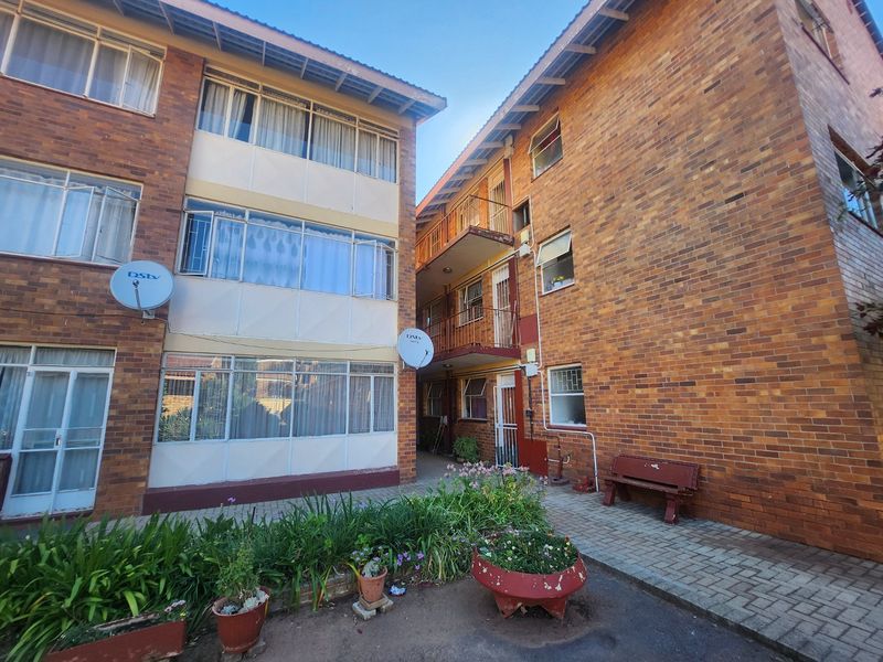 Exterior view of a multi-story apartment complex featuring face brick facades, metal balcony railings, and a paved communal courtyard area.