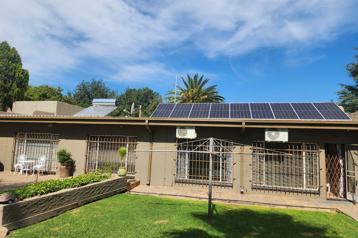 Rear exterior view of the house featuring solar panels, a solar water heater, wall-mounted air conditioning units, and security bars on windows.