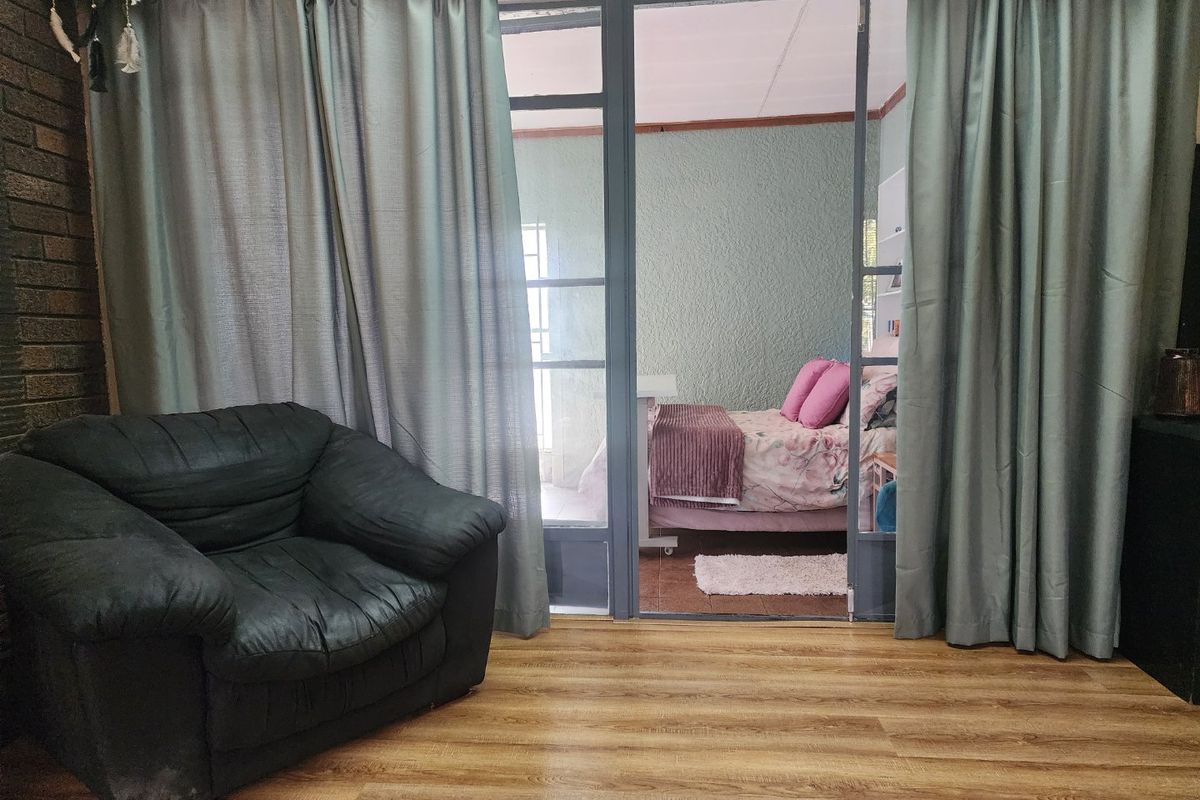 Living area featuring a brick accent wall and laminate flooring, with a glass-panelled door leading into an adjacent bedroom space.