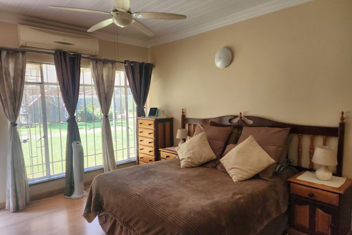 A comfortable bedroom featuring laminate flooring, a ceiling fan, and a split-system air conditioner, with large windows fitted with security bars.