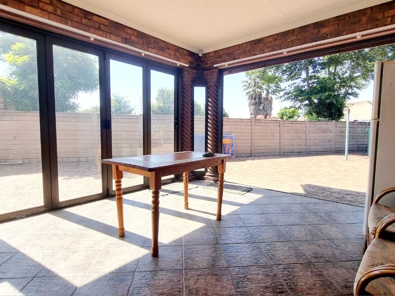A bright, enclosed patio area featuring tiled flooring, decorative brick accents, and large folding glass doors that open out to the rear garden.