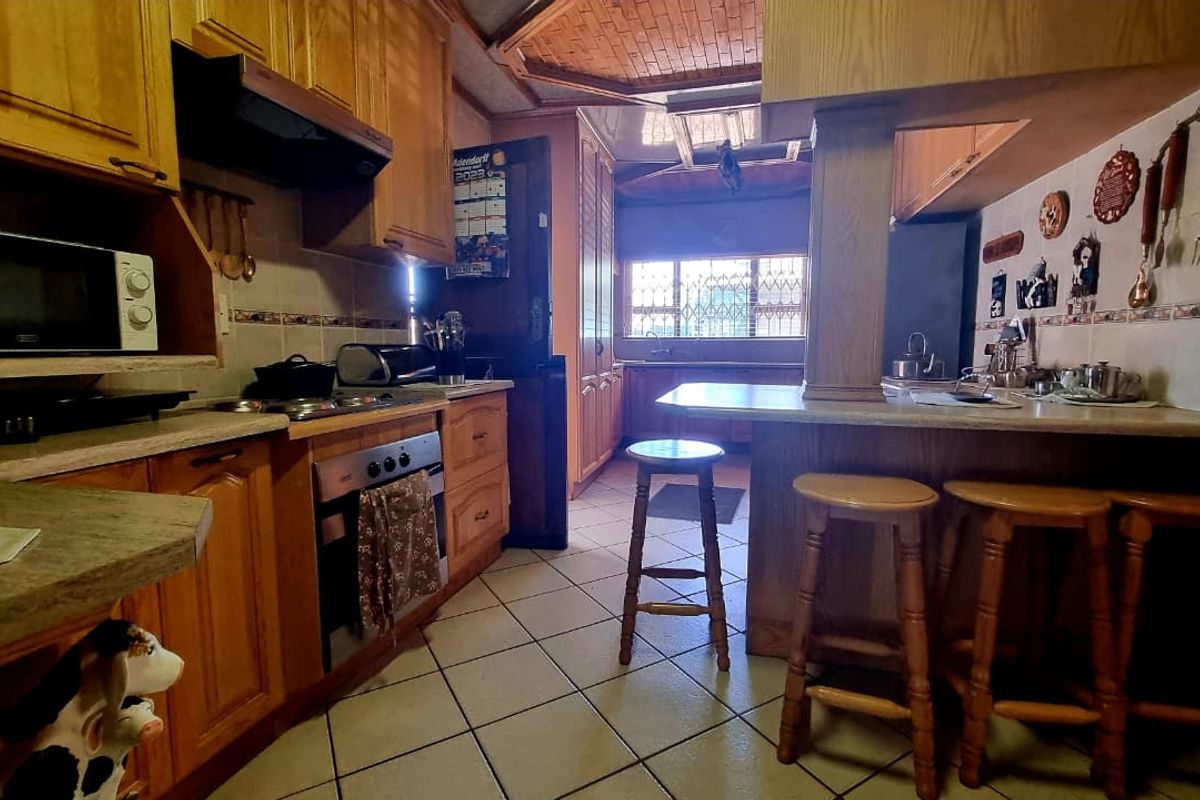 A traditional kitchen featuring extensive wooden cabinetry, a breakfast bar, built-in oven, and tiled flooring, offering a functional layout with classic finishes.