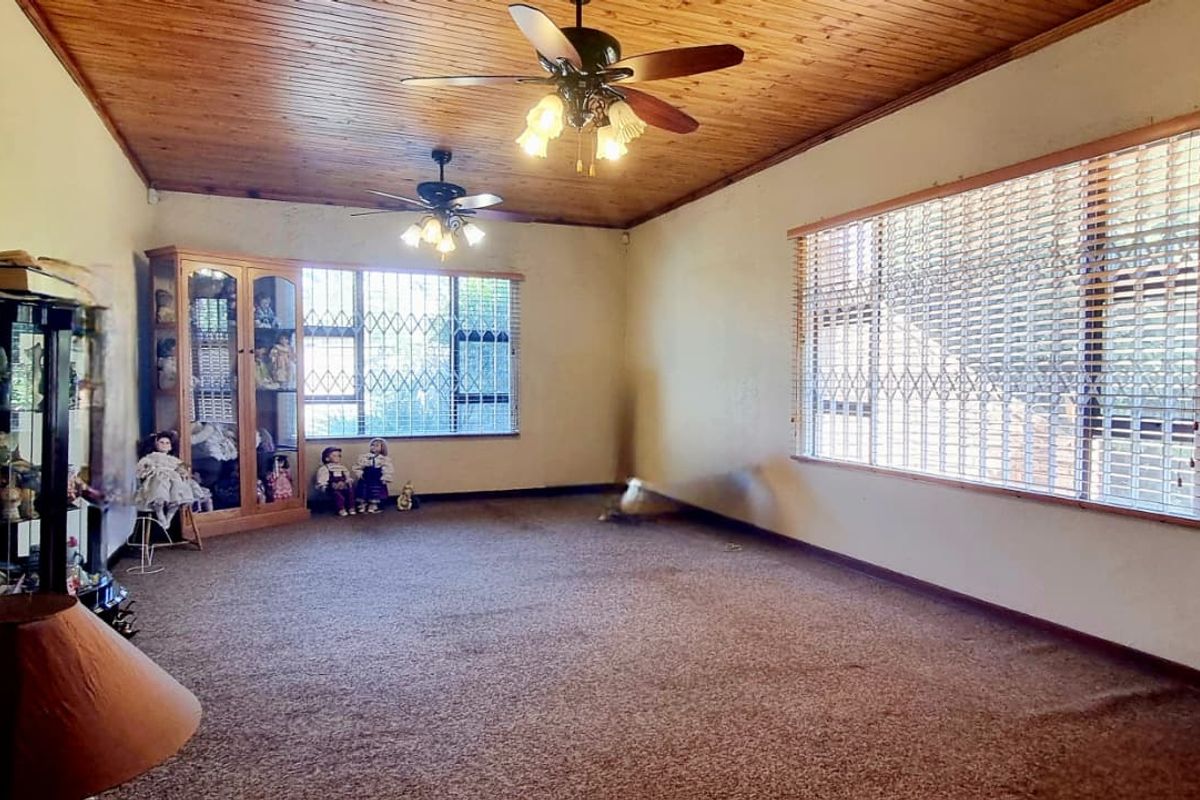 Spacious living room featuring a timber-clad ceiling, dual ceiling fans, and large windows fitted with security gates and blinds.