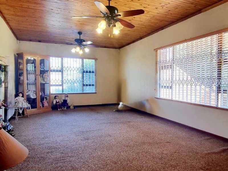 Spacious living room featuring a timber-clad ceiling, dual ceiling fans, and large windows fitted with security gates and blinds.
