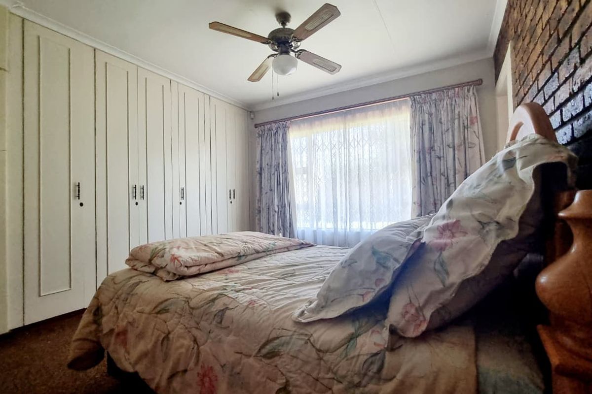 A bedroom featuring extensive built-in cupboards, a ceiling fan, and a characterful exposed brick feature wall.