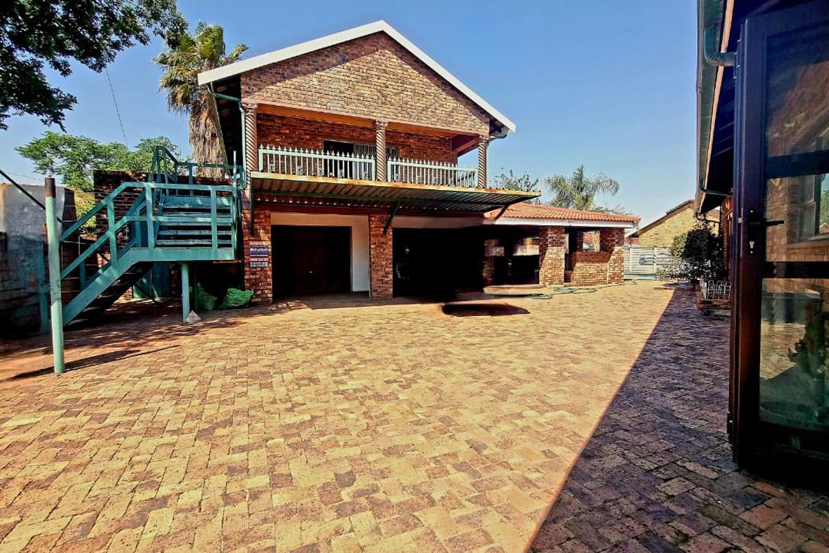 A spacious rear exterior area featuring a brick house facade, paved courtyard, external staircase leading to a balcony, and integrated garage access.
