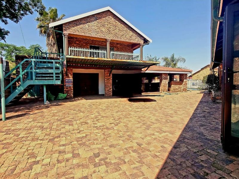 A spacious rear exterior area featuring a brick house facade, paved courtyard, external staircase leading to a balcony, and integrated garage access.