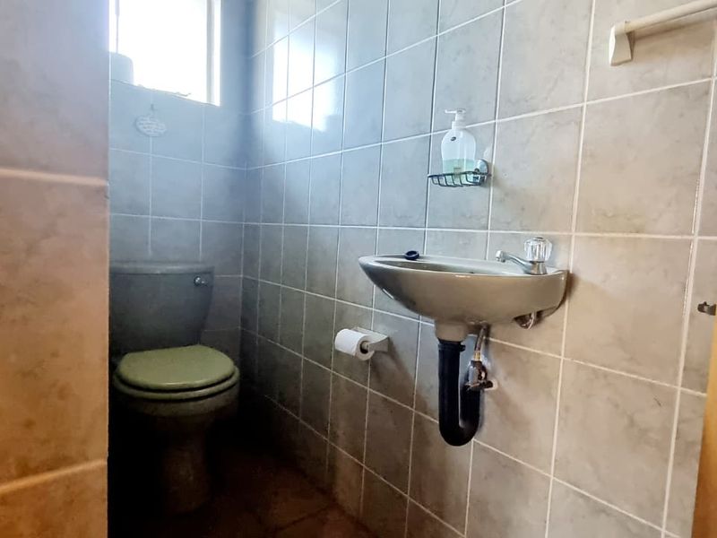 A compact bathroom featuring fully tiled walls, a wall-mounted basin, and a standard toilet.