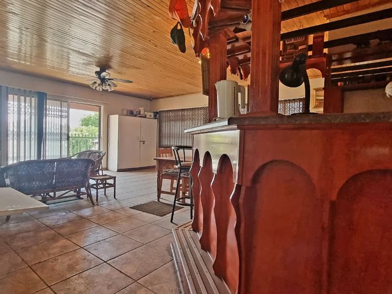 Spacious living area featuring a prominent built-in wooden bar, timber-clad ceiling, tiled flooring, and direct access to the outdoors via sliding glass doors.