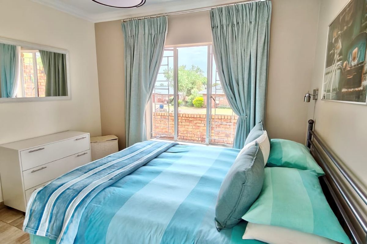 A well-maintained bedroom featuring tiled flooring, security bars on the window, and wall-mounted reading lights.