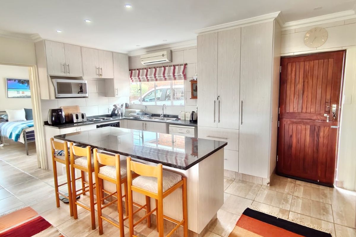 A well-maintained kitchen featuring a central island with granite countertops, ample built-in cabinetry, and tiled flooring, seamlessly connected to the adjacent living space.