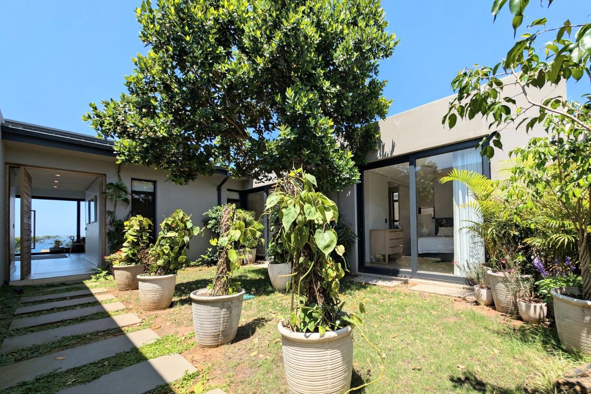 A private courtyard garden featuring a paved walkway, mature tree, and large sliding glass doors providing seamless indoor-outdoor flow.