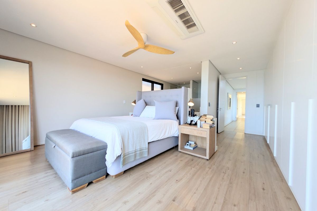 Modern bedroom featuring light wood-look laminate flooring, recessed ceiling lighting, a ceiling fan, integrated ducted air conditioning, and ample built-in storage.
