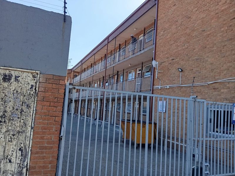 Exterior view of a multi-story apartment building featuring brick facade, metal security gate, and balconies with metal railings.