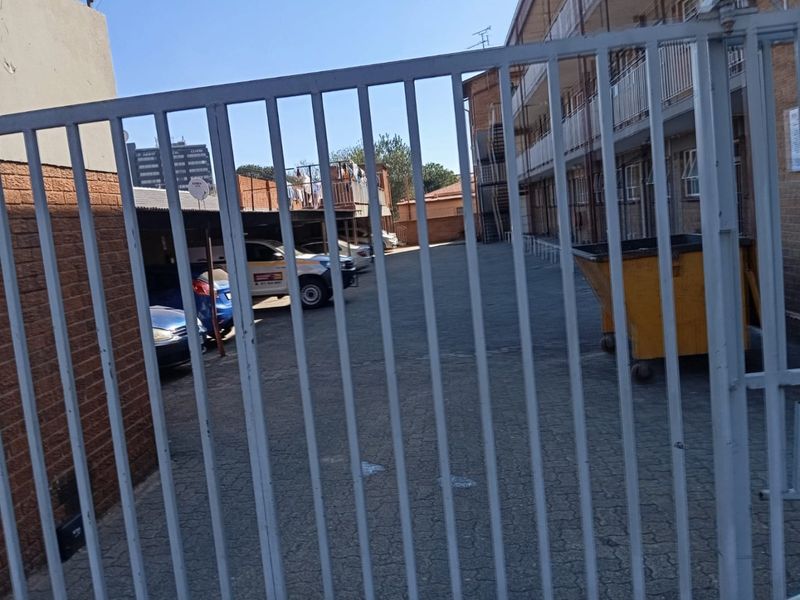 View of the apartment complex rear parking area, featuring paved driveway, covered carports, and secure metal gate access.