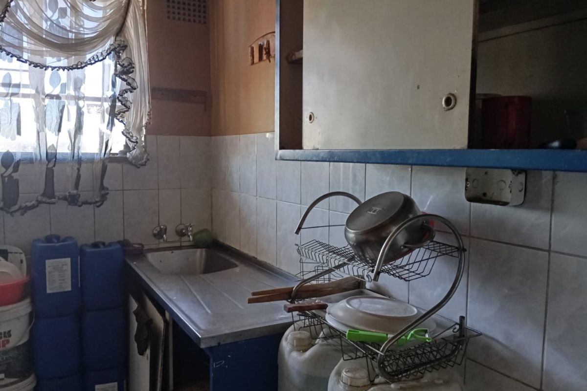 A dated kitchen area featuring a stainless steel sink, tiled splashback, and built-in cabinetry in need of renovation and modernization.