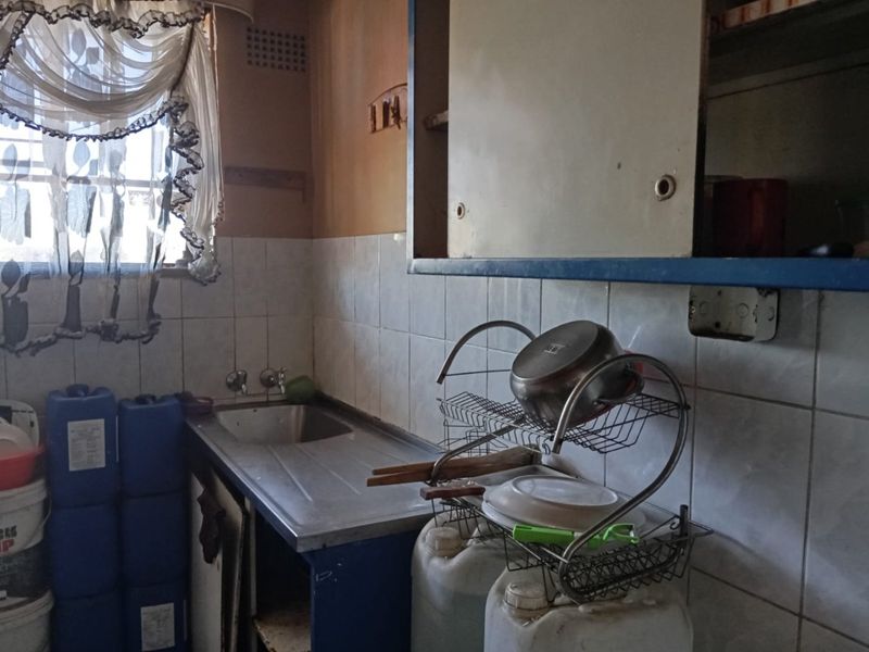 A dated kitchen area featuring a stainless steel sink, tiled splashback, and built-in cabinetry in need of renovation and modernization.