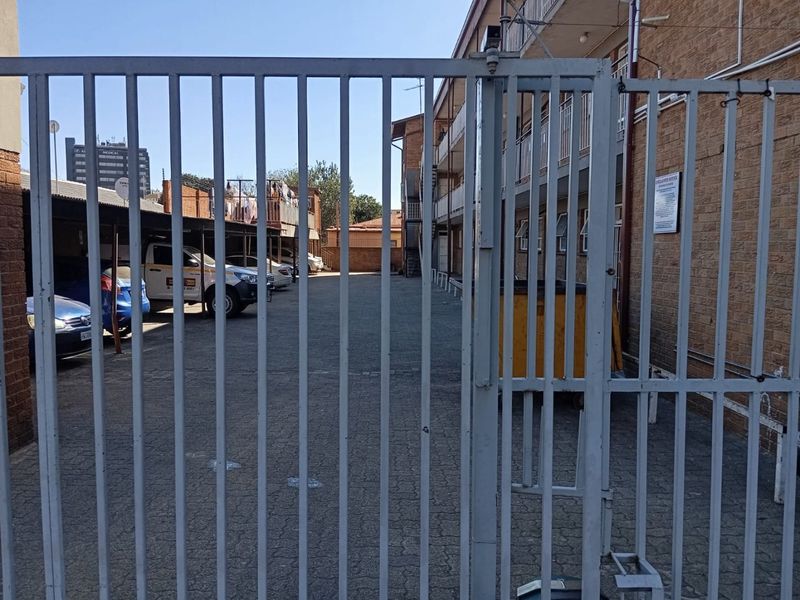 View of the apartment complex entrance featuring a metal security gate, paved driveway, and covered parking area.