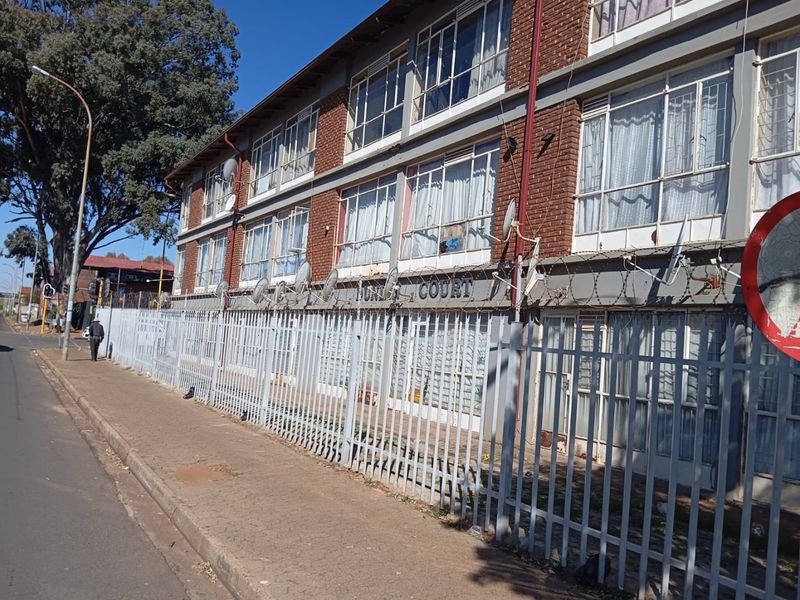 Street-level view of a multi-story brick apartment building featuring extensive steel security fencing and barbed wire perimeter protection.