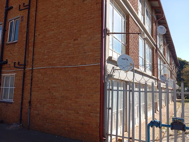 Exterior view of a multi-story apartment building featuring face brick construction, steel-framed windows, and perimeter security fencing with razor wire.