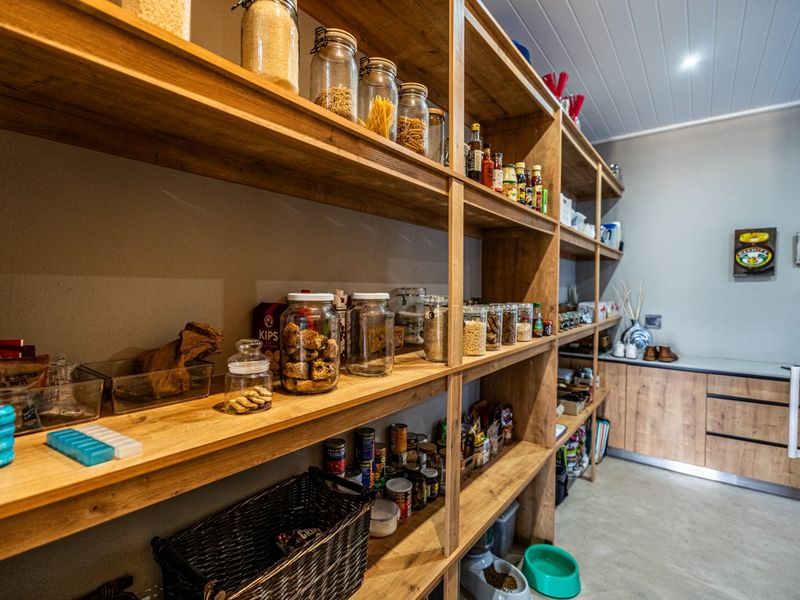 A well-organized scullery featuring extensive built-in timber shelving, laminate cabinetry, and durable concrete flooring, providing ample storage space.