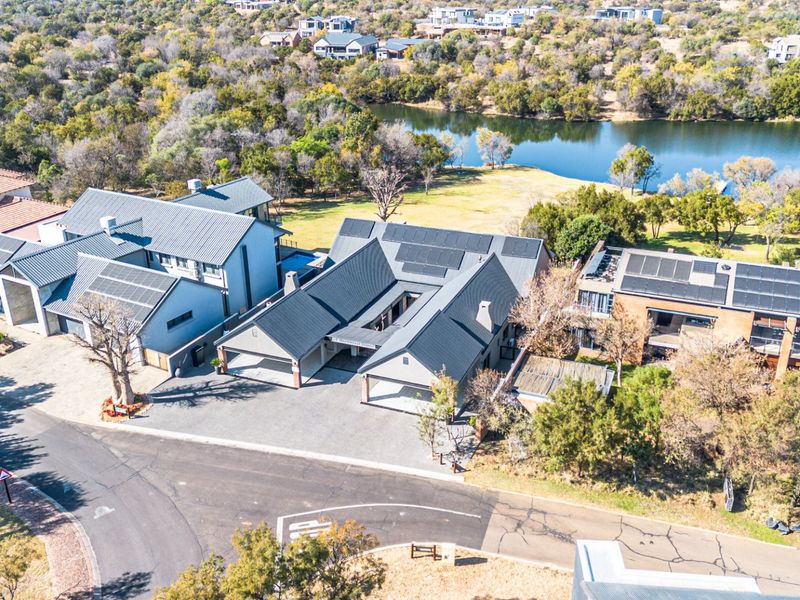 Aerial view of a modern residential property featuring multiple garage bays, extensive solar panel installations, and a metal roof, situated near a lake.